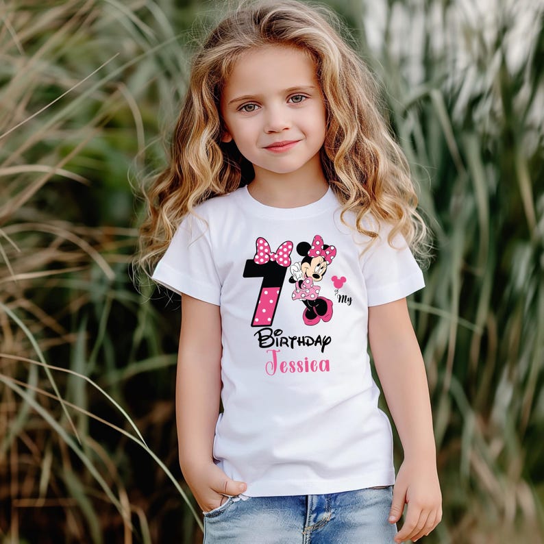Op de afbeelding: Een wit T-shirt met een Minnie Mouse-ontwerp, het nummer 7 in roze en zwarte stippen en de tekst "Birthday Jessica" in roze. Dit T-shirt is ontworpen voor een kinder verjaardagsfeestje.