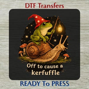 May include: A DTF transfer design with a green frog in a red wizard hat riding a snail, carrying a lantern. The design includes the text "Off to cause a kerfuffle" and "READY To PRESS". The image has a whimsical, fantasy theme.
