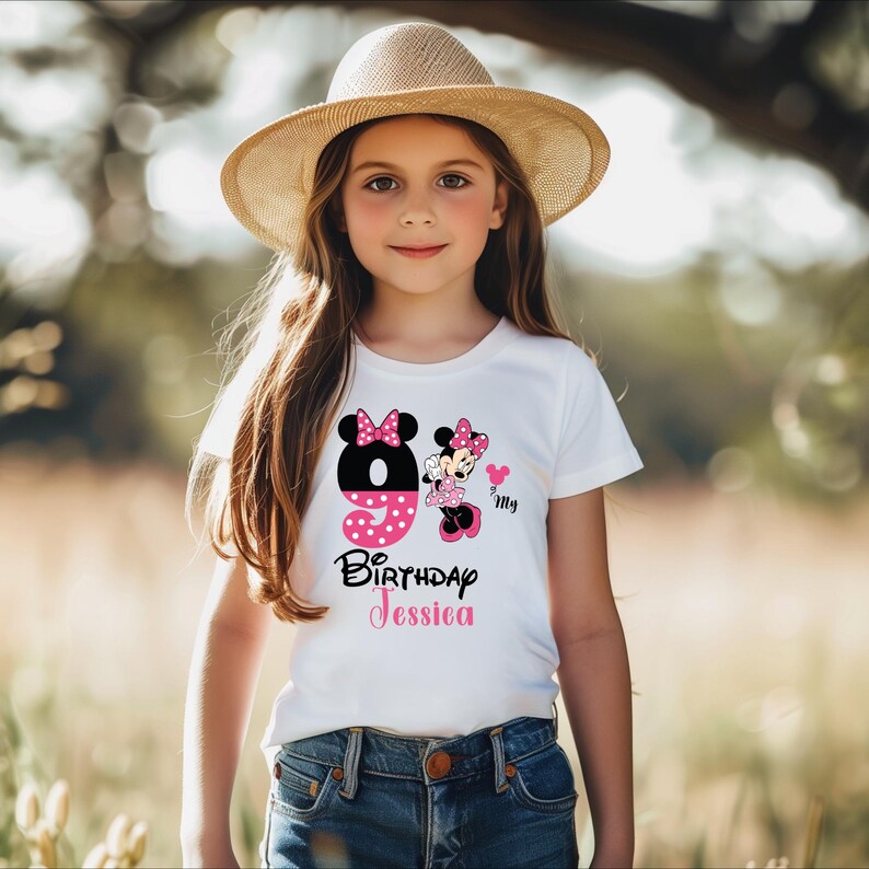Op de afbeelding: Een wit T-shirt met een Minnie Mouse-verjaardagsontwerp. Het ontwerp bevat het nummer 9, een Minnie Mouse-afbeelding en de tekst "Birthday Jessica". Het shirt wordt gedragen door een jong meisje dat een strohoed draagt.