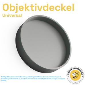 May include: A gray, circular Objektivdeckel, or lens cap, with a raised edge. The word "Universal" is above the product name. A logo with a cartoon bee and the words "Happy Bumblebee Creating Joy" is in the lower right corner.