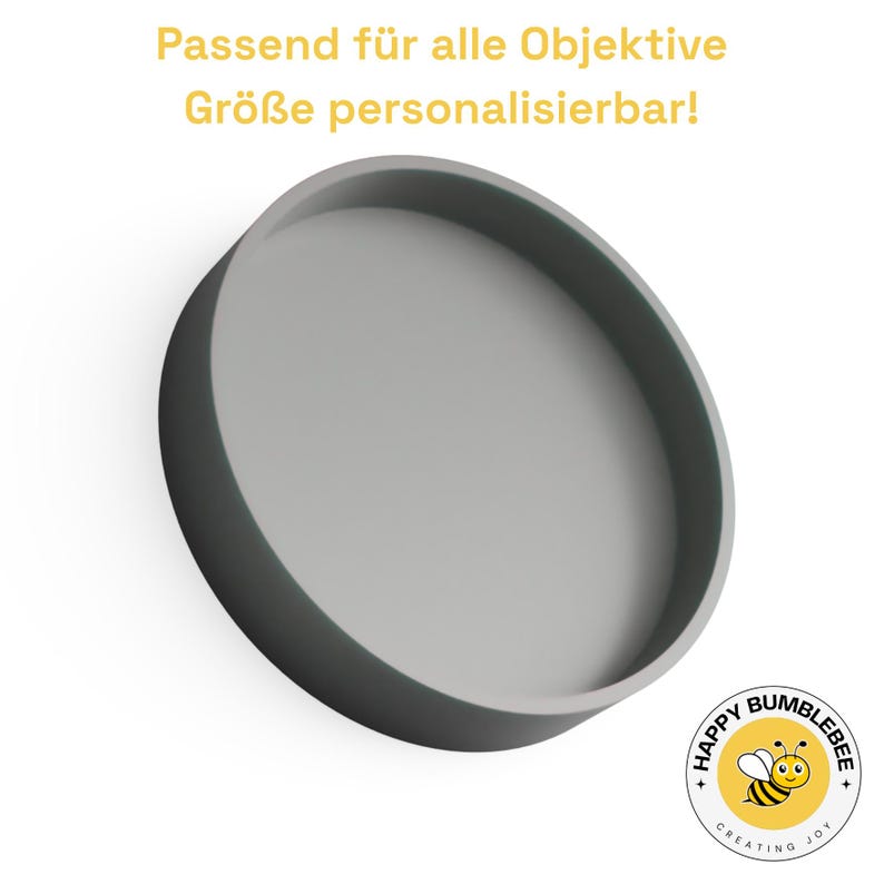 May include: A gray, circular tray with a raised edge. The text "Passend f&uuml;r alle Objektive Gr&ouml;&szlig;e personalisierbar!" is at the top. A logo with a cartoon bumblebee is in the bottom right corner.