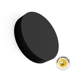 May include: A solid black, circular object with a slightly beveled edge. The object is set against a white background. A small, circular logo with a cartoon bee is in the lower right corner.