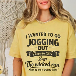 May include: Mustard yellow t-shirt with the text "I WANTED TO GO JOGGING BUT Proverbs 28:1 Says The wicked run when no one is chasing them." The shirt is a casual style.