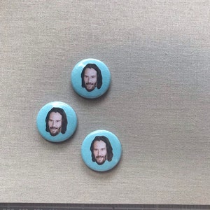 May include: Three blue round buttons featuring a picture of a man with long hair and a beard. The man is smiling and looking at the camera.
