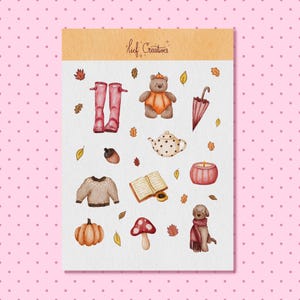 Op de afbeelding: Een stickervel met het opschrift Lief Creatives met aquarelillustraties van herfstitems, waaronder rode regenlaarzen, een beer in een pompoenpak, een paraplu, een theepot met stippen, een trui, een open boek, een kaars, een pompoen, een paddenstoel en een hond.