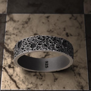 May include: A silver ring with a textured, cratered surface. The ring is marked with "925" on the inside.