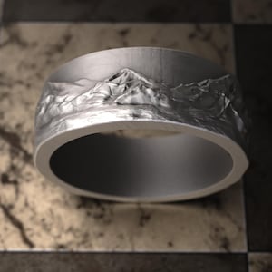 May include: A silver ring with a mountain range design. The ring is made of metal and has a smooth, polished finish.