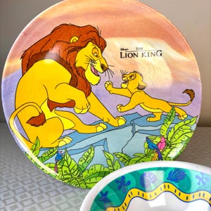 Op de afbeelding: Een ronde plaat met een sc&egrave;ne uit Disney's The Lion King, met Simba en Mufasa. De plaat heeft een kleurrijk ontwerp met een zonsondergangachtergrond en groen gebladerte. De plaat is geel, oranje en blauw.