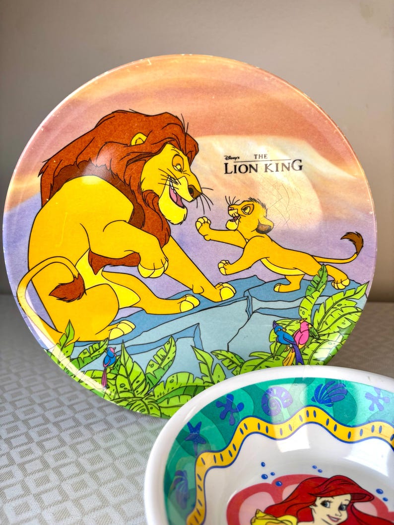 Op de afbeelding: Een ronde plaat met een sc&egrave;ne uit Disney's The Lion King, met Simba en Mufasa. De plaat heeft een kleurrijk ontwerp met een zonsondergangachtergrond en groen gebladerte. De plaat is geel, oranje en blauw.