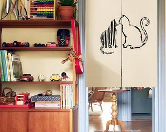 May include: Cream-colored door curtain with a black cat silhouette design. One cat is solid, the other is striped. The curtain hangs in a doorway, with a wooden table and shelves of toys and books visible in the background.