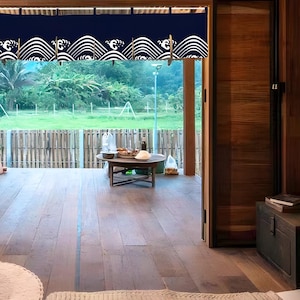 Puede incluir: Una puerta de madera con una cortina de patrón azul y blanco colgando sobre ella. La cortina tiene un diseño de onda. La puerta está abierta y hay un suelo de madera detrás de ella. Hay una mesa con algunos artículos sobre ella en el fondo.