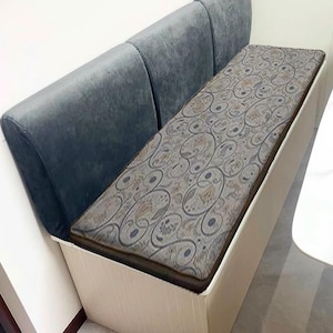 May include: A gray upholstered bench with three backrests and a patterned cushion. The bench has a light wood base with a storage compartment.