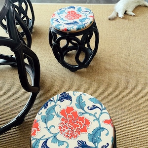 May include: Three black wooden stools with floral patterned cushions. The cushions are white with blue and red floral designs. The stools are arranged on a beige rug.