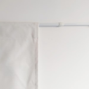 Op de afbeelding: Witte gordijnroede met witte eindkappen, hangend aan een witte muur. Een wit gordijn hangt aan de roede.