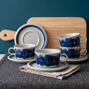 Peut inclure: Un ensemble de trois tasses à thé et soucoupes en céramique avec une base blanche et un motif floral bleu foncé. Les tasses ont une forme arrondie avec une anse, et les soucoupes présentent un bord bleu assorti. L'ensemble est posé sur une serviette.