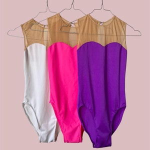 Puede incluir: Tres leotardos colgados de perchas. Los leotardos son blancos, rosas y morados. Cada leotardo tiene un panel de malla transparente en el escote.