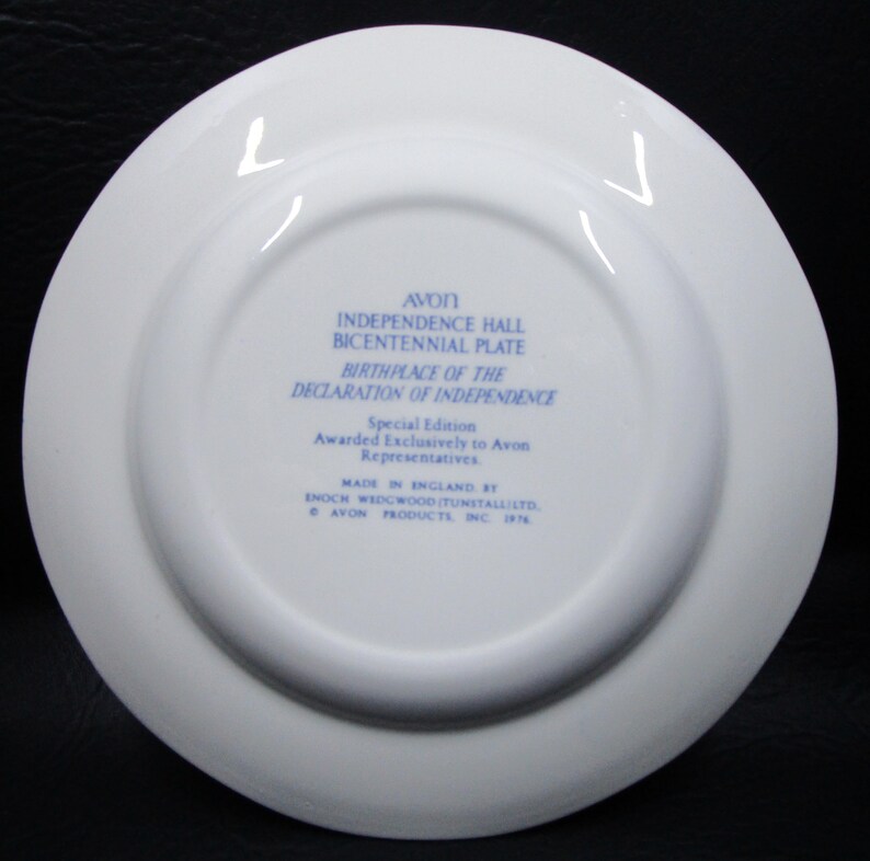 K&ouml;nnte beinhalten: Ein wei&szlig;er Keramikteller mit blauem Text. Der Text lautet "AVON INDEPENDENCE HALL BICENTENNIAL PLATE BIRTHPLACE OF THE DECLARATION OF INDEPENDENCE." Es ist eine Sonderausgabe, hergestellt in England von Enoch Wedgwood (Tunstall) Ltd.