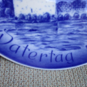 May include: Blue and white ceramic plate with the word "Vatertag" and the year "197..." in blue script.