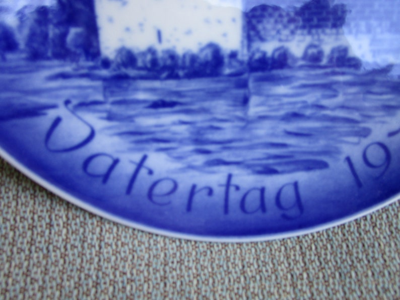 May include: Blue and white ceramic plate with the word "Vatertag" and the year "197..." in blue script.