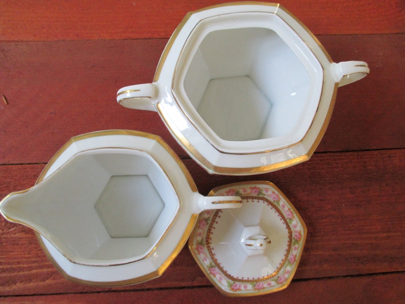 May include: A white porcelain creamer and sugar set with gold trim and a pink floral design on the lid. The creamer and sugar bowl are both octagonal in shape.