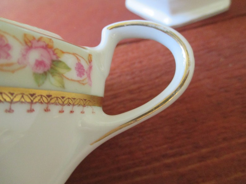 May include: A white porcelain creamer with a gold trim and floral design. The handle is also trimmed in gold.