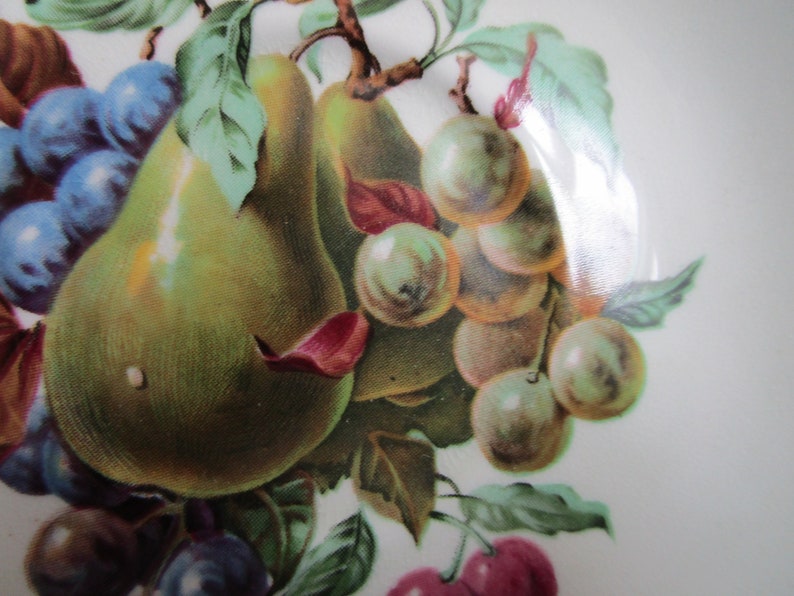 May include: A vintage ceramic plate with a hand-painted design of pears, grapes, and cherries. The pears are green and yellow, the grapes are purple and blue, and the cherries are red.