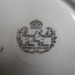 May include: Close-up of a white ceramic saucer with a black and white logo that reads "Royal Grafton Fine Bone China Made in England".