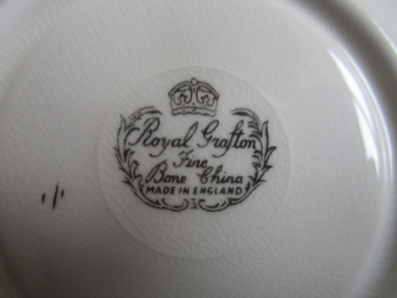 May include: Close-up of a white ceramic saucer with a black and white logo that reads "Royal Grafton Fine Bone China Made in England".