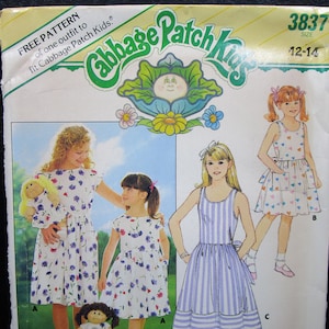May include: A Cabbage Patch Kids sewing pattern envelope 3837 for sizes 12-14. The cover features illustrations of three dresses with floral and striped patterns, along with a doll wearing a matching dress. The text reads Free Pattern.