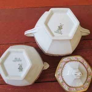 May include: Three white porcelain sugar bowls with gold trim. The bowls are octagonal in shape and have a floral design. The bottom of the bowls have a green and gold logo that reads "M.Z. Co. Hand Painted".