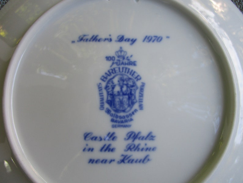 May include: A white ceramic plate with blue text and a blue logo. The text reads "Father's Day 1970", "100 Jahre Bareuther Porzellan", "Walboassen Bavaria Germany", "Castle Pfalz in the Rhine near Kaub".