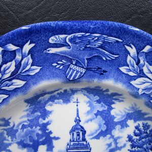 K&ouml;nnte beinhalten: Blaue und wei&szlig;e Zierteller mit einem Adler, Schild und Pfeilen sowie einem Kirchturm und Bl&auml;ttern. Der Teller hat ein detailliertes Design und eine klassische &Auml;sthetik, ideal zum Ausstellen oder Essen.