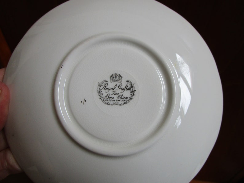May include: White saucer with a black and white Royal Grafton Bone China stamp. The stamp includes a crown and the words "Made in England".