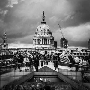 Puede incluir: Fotografía en blanco y negro de un puente lleno de gente que conduce a un gran edificio abovedado. El cielo está nublado. Una grúa de construcción es visible en el fondo.