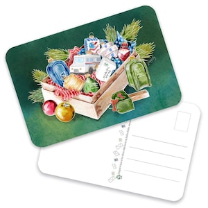 May include: Watercolor postcard featuring a wooden crate overflowing with Christmas ornaments, a postal truck, and a mailbox. The crate sits on a green background with a white postcard in the foreground. The ornaments are various colors and shapes.