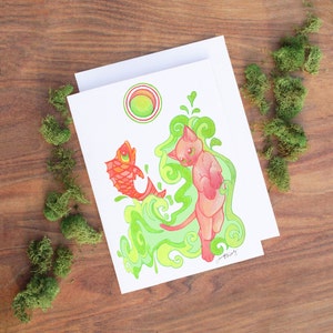 May include: A greeting card featuring a pink cat with a red fish and green swirling designs. The card has a circle with concentric rings in the upper left corner.