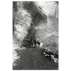 以下が含まれることがあります： 雪に覆われた狭い渓谷を馬に乗って進む2人のモノクロ写真。渓谷の壁は雪で覆われ、木々は裸です。ライダーは伝統的な衣装を着ています。