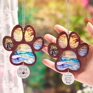 May include: Two wooden paw print ornaments with a beach scene design. Each ornament has a silver chain and a circular tag with text. One tag says "Peter" and the other says "I'm always with you Ruby".