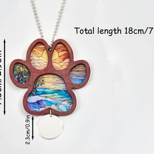 May include: A wooden paw print pendant with a beach scene design. The pendant is 2.95 inches wide and 7.08 inches long, including the chain. The paw print has a sunset and ocean design. A small, round, blank tag hangs below the paw print.