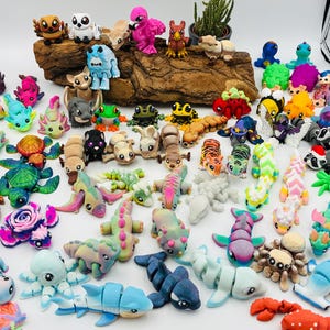 Könnte beinhalten: Eine Sammlung farbenfroher, handgefertigter Polymer-Tonfiguren, darunter Tiere, Kreaturen und Fantasiefiguren. Die Figuren haben verschiedene Formen und Größen, mit detaillierten Merkmalen und leuchtenden Farben. Einige befinden sich auf einem Holzstück.