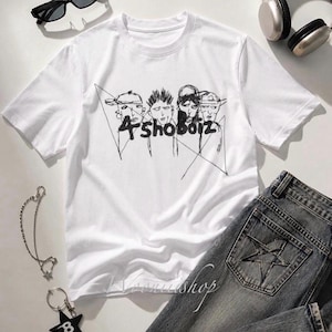 May include: A white short-sleeved t-shirt featuring a black line-art graphic of four figures wearing caps and the text 4shoboiz. The shirt is displayed with black sunglasses, silver headphones, a star-shaped keychain, and grey denim jeans.