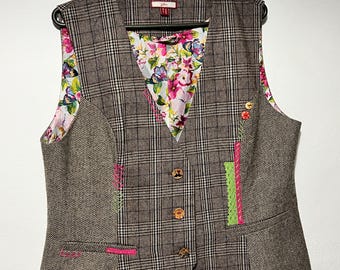 May include: A brown and black plaid vest with a floral lining and colorful embroidery details. The vest has a V-neck and four buttons down the front.