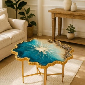 Puede incluir: Una mesa de centro única con base de metal dorado y tapa de resina. La tapa presenta un diseño azul y blanco con borde dorado y pequeñas piedras. La mesa mide aproximadamente 76 cm de largo.