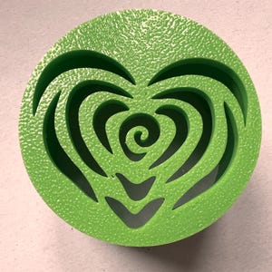 Op de afbeelding: Een groen rond object met een hartvormige uitsparing. Het hart is gevuld met een draaiend patroon.