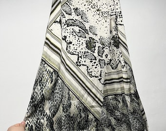 May include: A flowing, asymmetrical skirt with a snakeskin print in shades of black, white, and olive green. The skirt is hanging on a black hanger. The fabric has a silky sheen.
