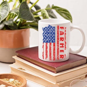 May include: White ceramic mug featuring a distressed American flag design with the word "FARMER" in red. The mug is set on a stack of books, with a plant in the background. A patriotic themed gift.
