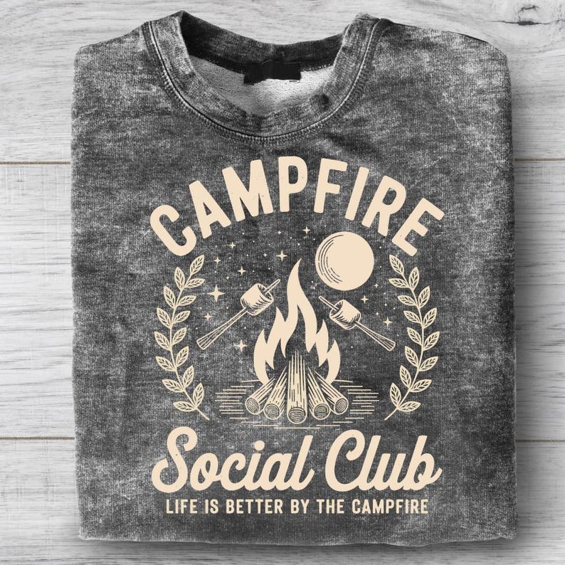May include: A dark gray sweatshirt with a graphic design featuring the words "Campfire Social Club." The design includes a campfire, marshmallows, and the text "Life is better by the campfire."