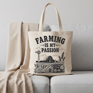 May include: Cream-colored tote bag with the text "FARMING IS MY PASSION" in a black, vintage font. The design includes a tractor, barn, windmill, and wheat stalks, all in black and white. The bag has a simple, rectangular shape.