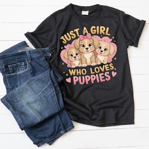 May include: A black t-shirt with the text "JUST A GIRL WHO LOVES PUPPIES" and a graphic of three puppies inside a pink heart. The shirt is paired with a pair of blue jeans.