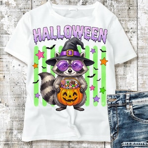 May include: A white t-shirt featuring a graphic of a raccoon wearing a black witch hat and purple round glasses. The raccoon holds an orange jack-o'-lantern bucket filled with candy. The word HALLOWEEN is printed in purple above the raccoon.